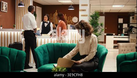 Der Hotelmanager ist beschäftigt und erhält eine Tasse Kaffee vom Mitarbeiter, während er die Papiere der Gäste überprüft, die auf den Check-in warten. Der Rezeptionist bietet Pärchen nach Abschluss der Buchung Zugang zum Zimmer Stockfoto