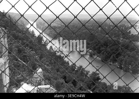 Historischer Archivblick von Slavyanogorsk (heute Sviatohirsk) aus dem Jahr 1956 mit Blick auf das malerische Tal des Siwerskyi Donets. Die Szene fängt eine Hochwinkelperspektive ein, die durch einen Drahtzaun aus Diamantgewebe hinunterblickt und kleine Ruderboote enthüllt, die durch das ruhige Wasser inmitten von dichten Sommerwäldern navigieren. Diese nostalgische Landschaft aus der Mitte des zwanzigsten Jahrhunderts zeigt die natürliche Schönheit und die Outdoor-Freizeitkultur der Sowjetzeit, wobei die historische Umgebung und das topografische Erbe der Region erhalten bleiben und den friedlichen Donbass widerspiegeln. Stockfoto