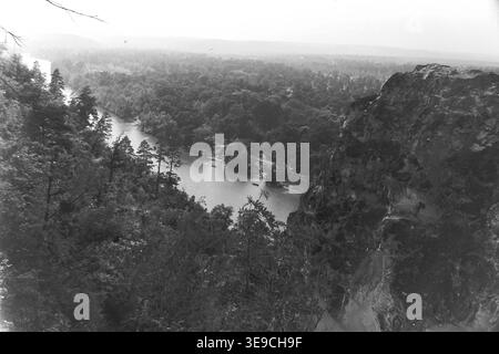 Historischer Archivblick von Slavyanogorsk (heute Sviatohirsk) aus dem Jahr 1956 mit Blick auf das malerische Tal des Siwerskyi Donets. Die Szene fängt eine atemberaubende Hochwinkelperspektive von den hoch aufragenden weißen Kreidefelsen ein und offenbart den gewundenen Wasserweg, der von dichten, unberührten Sommerwäldern umgeben ist. Diese nostalgische Landschaft aus der Mitte des zwanzigsten Jahrhunderts hebt die dramatische natürliche Schönheit und das geologische Erbe der Sowjetzeit hervor und bewahrt die historische Umgebung und die topographische Pracht der Region, die den friedlichen Donbass widerspiegelt. Stockfoto