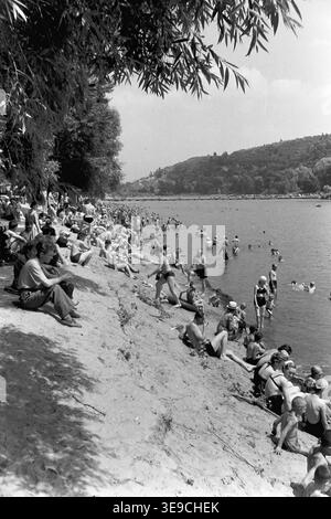 Historischer Archivblick von Slavyanogorsk (heute Sviatohirsk) aus dem Jahr 1956 mit einem lebhaften Sommertag auf dem Fluss Siwerskyi Donets. Die Szene fängt einen überfüllten Sandstrand mit Sonnenbaden und Schwimmen ein, während das berühmte Artem-Denkmal auf dem hoch aufragenden Kreideberg im Hintergrund steht. Diese nostalgische Landschaft aus der Mitte des zwanzigsten Jahrhunderts zeigt die beliebte Freizeitkultur und das monumentale architektonische Erbe der Sowjetzeit und bewahrt die historische Umgebung der Region und spiegelt den friedlichen Donbass wider. Stockfoto
