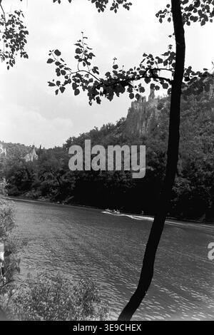 Historischer Archivblick von Slavyanogorsk (heute Sviatohirsk) aus dem Jahr 1956 mit Blick auf den malerischen Fluss Siwerskyi Donets, der von dunklen Baumsilhouetten eingerahmt wird. Die Szene fängt kleine Ruderboote und eine Passagier-Flussbahn auf dem Wasser ein, während die majestätische Kreidekirche St. Nikolaus auf der Klippe im Hintergrund aufsteigt. Diese nostalgische Landschaft aus der Mitte des zwanzigsten Jahrhunderts hebt die natürliche Schönheit und das architektonische Erbe der Sowjetzeit hervor und bewahrt die historische Umgebung der Region und spiegelt den friedlichen Donbass wider. Stockfoto