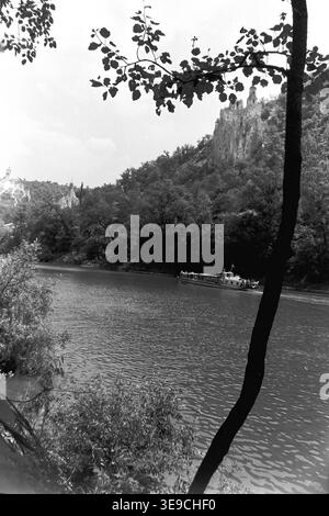 Historischer Archivblick von Slavyanogorsk (heute Sviatohirsk) aus dem Jahr 1956 mit Blick auf den malerischen Fluss Siwerskyi Donets, der von dunklen Baumsilhouetten eingerahmt wird. Die Szene fängt kleine Ruderboote und eine Passagier-Flussbahn auf dem Wasser ein, während die majestätische Kreidekirche St. Nikolaus auf der Klippe im Hintergrund aufsteigt. Diese nostalgische Landschaft aus der Mitte des zwanzigsten Jahrhunderts hebt die natürliche Schönheit und das architektonische Erbe der Sowjetzeit hervor und bewahrt die historische Umgebung der Region und spiegelt den friedlichen Donbass wider. Stockfoto