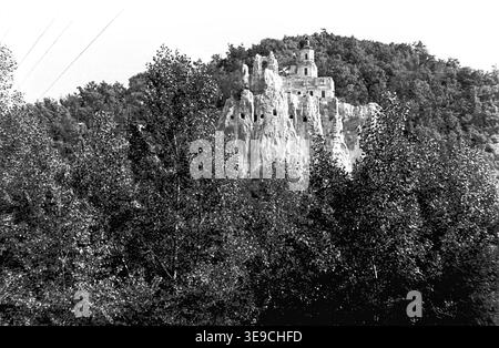 Historische Archivansicht von Slavyanogorsk (heute Sviatohirsk) aus dem Jahr 1956, die das bemerkenswerte architektonische und geologische Erbe der Region zeigt. Die Szene zeigt eine detaillierte Perspektive auf die historische Nikolaikirche, die direkt in die hohen weißen Kreidefelsen gehauen wurde und von dichtem Sommerlaub umgeben ist. Diese nostalgische Landschaft aus der Mitte des zwanzigsten Jahrhunderts zeigt die einzigartigen religiösen Strukturen, Handwerkskunst und natürliche Schönheit der Sowjetzeit und bewahrt die historische Umgebung der Region und spiegelt den friedlichen Donbass wider. Stockfoto