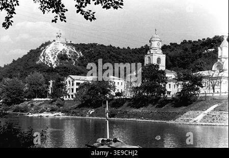 Historischer Blick aus dem Jahr 1956 auf Slavyanogorsk (heute Sviatohirsk), der das herrliche architektonische Erbe entlang des Siwerskyi Donets-Flusses zeigt. Die Szene zeigt die historischen Gebäude von Svyatogorsk Lavra, einschließlich der Pokrowskaja Kirche mit ihrem Uhrenturm, die sich vor dem bewaldeten Kreideberg und dem Artem-Denkmal befindet. Diese nostalgische Landschaft aus der Mitte des zwanzigsten Jahrhunderts zeigt die religiöse Geschichte, monumentale Kunst und natürliche Schönheit der Sowjetzeit und bewahrt die historische Umgebung der Region, die den friedlichen Donbass widerspiegelt. Stockfoto