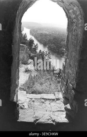 Historischer Archivblick von Slavyanogorsk (heute Sviatohirsk) aus dem Jahr 1956 mit atemberaubender Aussicht auf das Tal des Siwerskyi Donets. Die Szene ist wunderschön eingerahmt durch ein rustikales, bogenförmiges Steinfenster einer historischen Ruine an den Klippen, die den gewundenen Wasserweg, kleine Boote und dichte, üppige Sommerwälder enthüllt. Diese nostalgische Landschaft aus der Mitte des zwanzigsten Jahrhunderts hebt das architektonische Erbe, die natürliche Schönheit und die romantischen Ausblicke der Sowjetzeit hervor und bewahrt die historische Umgebung der Region, die den friedlichen Donbass widerspiegelt. Stockfoto