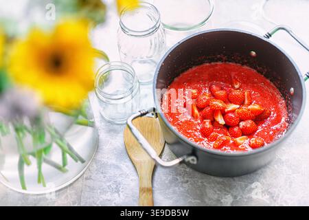 Ein Topf auf einem Herd mit sprudelnder Erdbeermarmelade, die mit einem Löffel gerührt wird. Hausgemachte Erdbeermarmelade. Stockfoto