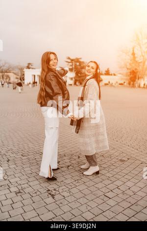 Friends Walking plaza zwei junge Frauen halten Hände und lächeln, während sie an einem sonnigen Herbstnachmittag durch einen Stadtplatz laufen Stockfoto