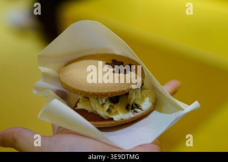 Handheld Ice Cream Sandwich mit Plätzchen und Schokoladenchips in Papier auf gelbem Hintergrund gewickelt Stockfoto