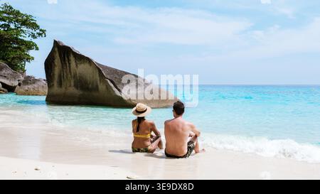 Ein abwechslungsreiches Paar sitzt friedlich am Sandstrand der Similan Islands, umgeben von klarem türkisfarbenem Wasser und atemberaubenden Felsformationen. Diese idyllische Umgebung ist perfekt für Romantik und Entspannung. Stockfoto