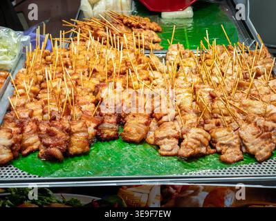 Traditionelles thailändisches Street Food mit einem großen Haufen süßer gegrillter Schweinespieße auf einem grünen Bananenblatt auf einem lokalen Markt. Stockfoto