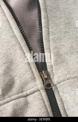 Schwarzer Reißverschluss auf grauem, meliertem Fleecestoff mit Metallschieber aus Bronze, Draufsicht auf das Modedesign-Konzept der Bekleidungskonstruktion mit Kopierraum Stockfoto