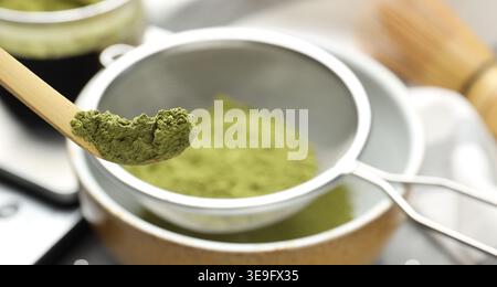 Matcha-Pulver in Schüssel auf grauem Tisch sieben, Nahaufnahme Stockfoto