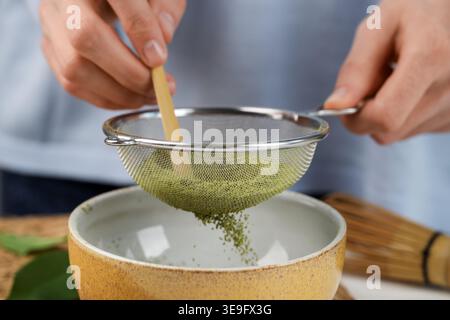 Frau, die Matcha-Pulver in eine Schüssel am Tisch siebt, Nahaufnahme Stockfoto