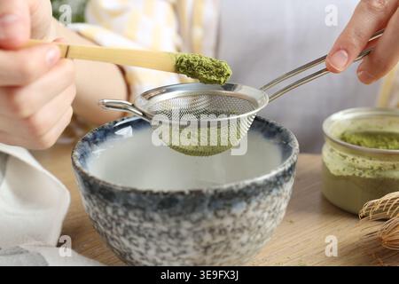 Frau, die Matcha-Pulver in eine Schüssel am Holztisch siebt, Nahaufnahme Stockfoto