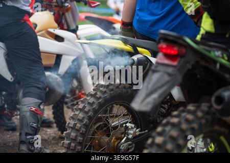 Eine Nahaufnahme von blauem Rauch, der aus einem Schmutzfahrrad-Auspuffrohr kommt. Das Bild erfasst den Moment vor dem Start eines Motocross- oder Enduro-Rennens, wi Stockfoto