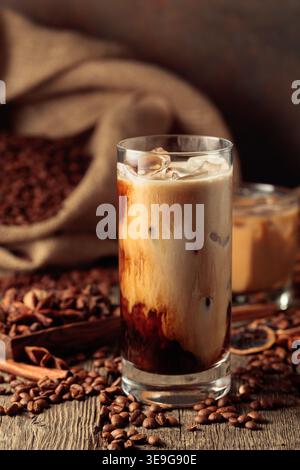 Eiskaffee mit Sahne. Auf einem alten Holztisch liegt eine Tüte gerösteter Kaffeebohnen und über den Tisch verteilt sind Zimtstangen, Muskatnuss und ein Stockfoto