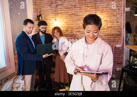 Junge asiatische Geschäftsfrau mit Tablet und Kollegen im Hintergrund Stockfoto