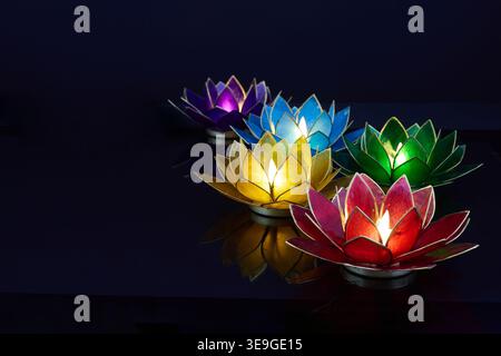 Vesak. Farbenfrohe Lotusblüten-Teelicht-Kerzen, die in dunklem Wasser leuchten Stockfoto