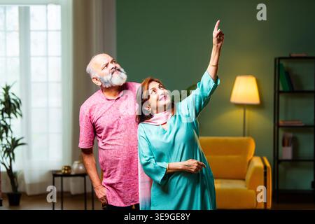 Eine Rückansicht eines älteren indischen Paares, das in ihrem Wohnzimmer steht und in die Ferne zeigt. Der pensionierte Ehemann und die Frau teilen einen Moment Stockfoto