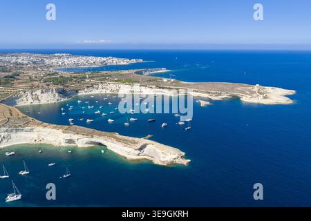 Blick aus der Vogelperspektive auf den St. Peters Pool in der Nähe von Marsaxlokk mit Kalksteinklippen, türkisfarbener Bucht und Booten auf dem Mittelmeer. Stockfoto