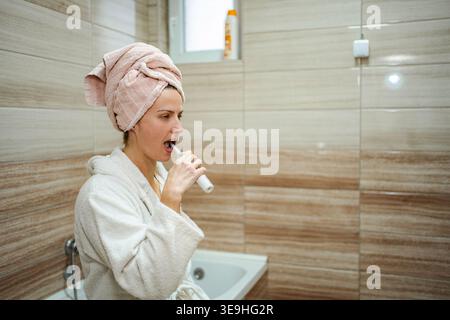 Frau putzt im Badezimmer Zähne mit Bademantel und Handtuch Stockfoto