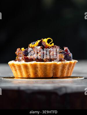Goldene Tarte sitzt elegant auf dunkler Oberfläche. Knusprige Kruste hält eine reichhaltige, klobige Fruchtfüllung. Die Zitrusschale sorgt für ein helles, aromatisches Finish. Tiefe Schatten fra Stockfoto