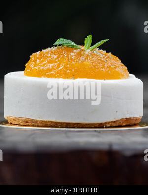 Weißes Dessert ruht auf dunkler Holzoberfläche. Orangefarbene Glasur mit Minzblättern sorgt für einen lebendigen Kontrast. Die bröckelige Basis sorgt für eine reichhaltige, verwöhnende Textur. Stockfoto