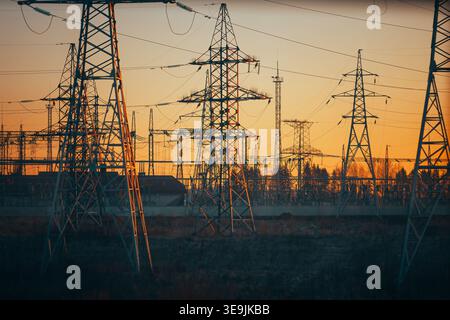 Elektrische Übertragungsleitungen und Pylonen, Silhouetten vor Sonnenuntergang, industrielle Energieinfrastruktur. Stockfoto