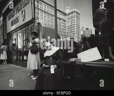Historisches Foto mit dem Titel nun, das vor einem Schaufenster sitzt und eine katholische Nonne auf einem Bürgersteig der Stadt zeigt, während Fußgänger in der Nähe vor einer Ladenfront stehen. Foto von Angelo Rizzuto, August 1958 Stockfoto