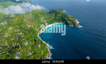 Ein üppig grüner Hügel mit Blick auf eine türkisfarbene Bucht mit klarem Wasser und sanften Wellen. Seychellen, Mahe. Stockfoto