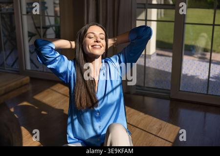 Frau sitzt auf sonnendurchflutetem Boden und genießt zu Hause Entspannung Stockfoto