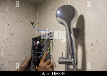 Professioneller Klempner, der Wassererhitzer in modernen Badezimmern installiert, konzentriert sich auf elektrische Kabelverbindungen und zeigt viel Engagement für Sicherheit und präzises Arbeiten Stockfoto