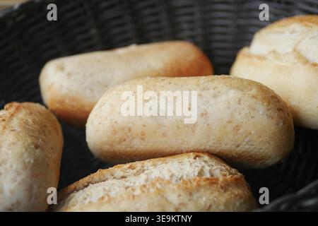 Frisch gebackene Brötchen in einem gewebten Korb auf einem Tisch Stockfoto
