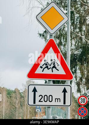 Riga, Lettland - 17. April, 2026: Straßensicherheitsschilder mit Warnhinweisen für das Überqueren von Kindern und einer vorrangigen Straßenmarkierung mit 200 m Entfernung. Ideal für Stockfoto