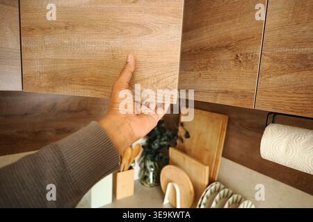 Person, die eine Holzschranktür in einem Küchenbereich öffnet Stockfoto