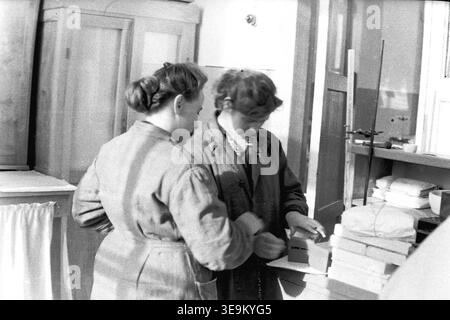 Slawjansk, 1950er Jahre AIZ-Werk. Ein wunderschönes historisches Schwarzweiß-Archivfoto, das zwei sowjetische Arbeiter in einer Produktionsanlage zeigt. Im Vordergrund steht die Arbeiterin Valentina Timofeevna Kravelis, die spezielle technische Ausrüstung hält, die die Frauen gemeinsam sorgfältig überprüfen. Dieses authentische Bild vermittelt lebendig Momente der Interaktion am Arbeitsplatz, typische Industriekleidung und aufrichtige zwischenmenschliche Kommunikation in einem großen sowjetischen Unternehmen und demonstriert den Alltag und den friedlichen Donbass. Stockfoto