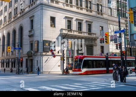 Toronto, Kanada - 17. April 2026: Straßenbahnen passieren historische Bauwerke, während Fußgänger an den Straßenübergängen in lebendigem Ambiente warten Stockfoto