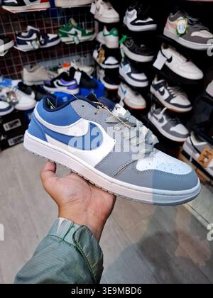 Hand, die einen modernen blau-weißen Sneaker in einem Schuhgeschäft mit unscharfem Hintergrund hält Stockfoto