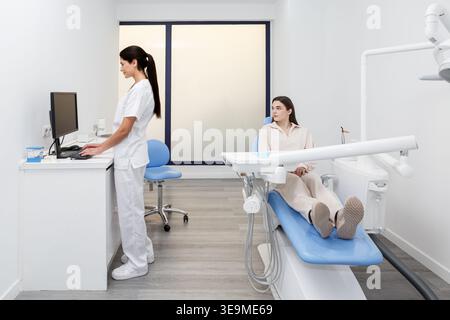 Ein Zahnarzt konzentriert sich auf einen Computer, während ein Patient in einem Zahnarztstuhl in einer modernen Klinik wartet. Diese Einstellung unterstreicht die Bedeutung der zahnärztlichen Versorgung a Stockfoto
