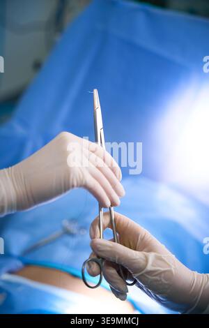 Zwei Hände in weißen Handschuhen, die chirurgische Instrumente in Innenräumen halten Stockfoto