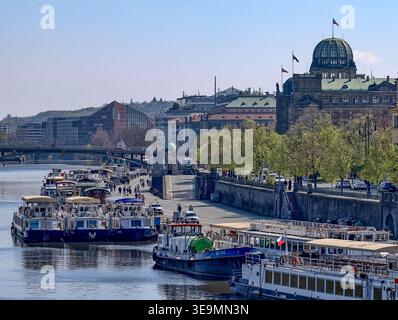 Prag, Tschechische Republik - 17. April 2026: Flussszene der Moldau mit Ausflugsbooten, Fußgängerzonen und historischem Kuppelgebäude Stockfoto