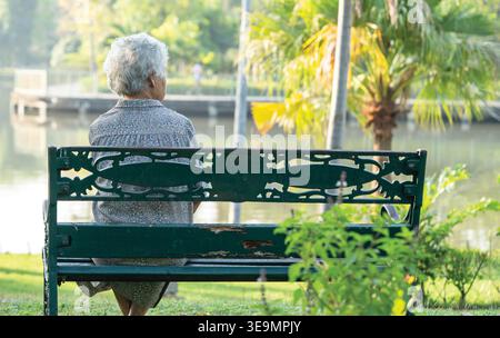 Asiatische ältere Frau deprimiert und traurig sitzen zurück auf Bank im Herbst Park. Stockfoto