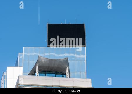 Modernes Gebäude mit großem Digitalbildschirm auf dem Dach vor blauem Himmel. Stockfoto