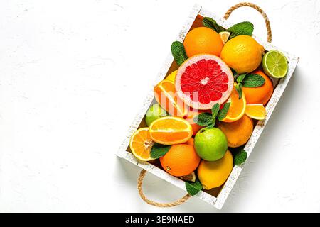 Frische Zitrusfrüchte mit Blättern: Zitronen, Orangen, Mandarinen, Grapefruit, Limette in Holzkiste, Draufsicht. Stockfoto