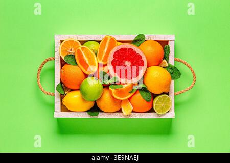 Frische Zitrusfrüchte mit Blättern: Zitronen, Orangen, Mandarinen, Grapefruit, Limette in Holzkiste, Draufsicht. Stockfoto