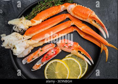 Luxuriöse kamtschatka-Krabbenbeine mit Zitronenscheiben und frischen Kräutern auf dunklem Teller Gourmet-Meeresfrüchte auf strukturiertem schwarzem Hintergrund. Stockfoto