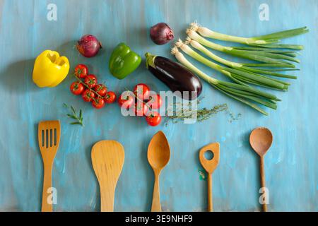 Holzlöffel und frisches Gemüse auf blauem Hintergrund Stockfoto