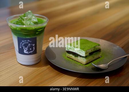 Matcha Latte und Matcha Tiramisu Slice auf Teller mit Löffel auf Holztisch Stockfoto