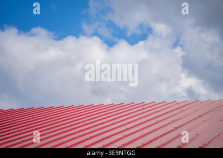 Flacher Winkel des roten Rippendachs mit Befestigungslinien unter bewölktem Himmel für Lagerbau, Außenverkleidung und Dachdesign Stockfoto