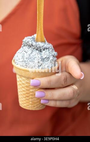 Helles Eis mit dunklen Krümeln wird in einem Waffelkegel serviert und von Frauenhand gehalten Stockfoto